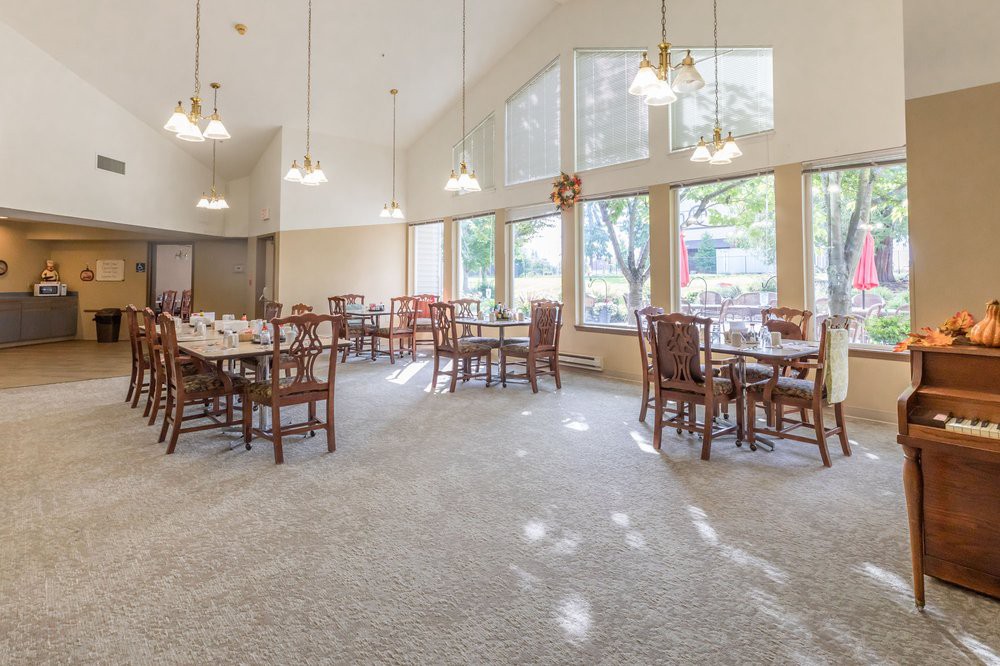 A spacious dining area with multiple tables and chairs, large windows, and hanging lights.
