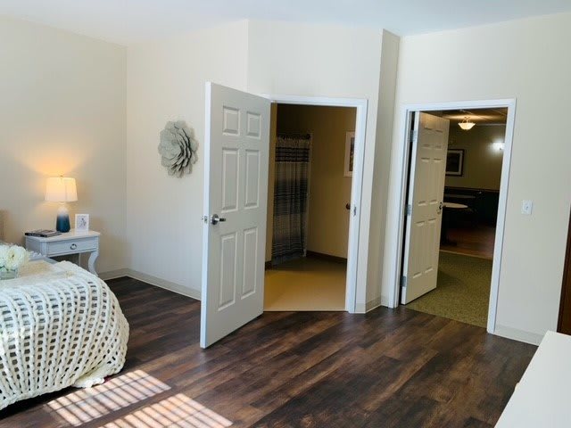 A cozy bedroom with an open door leading to a walk-in closet and another room, featuring wooden floors and soft lighting.