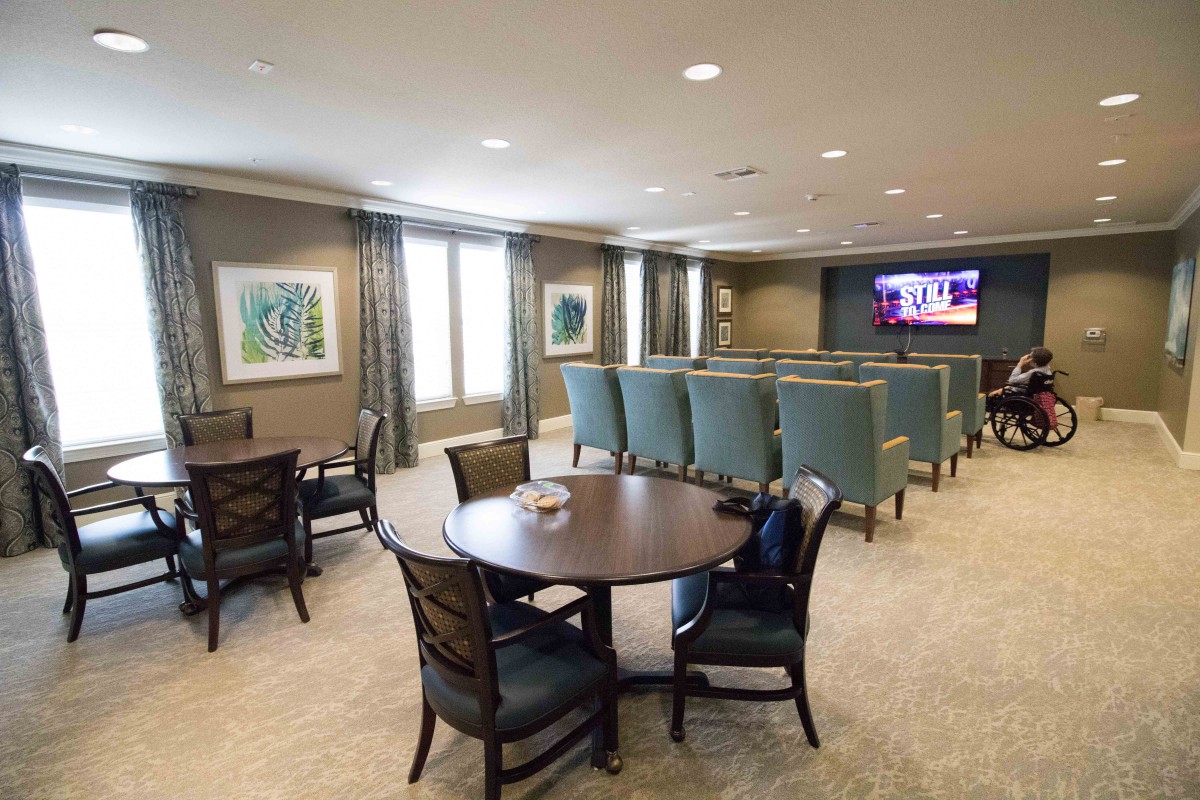 A spacious room featuring multiple seating areas with tables and chairs, a large screen television, and decorated walls.