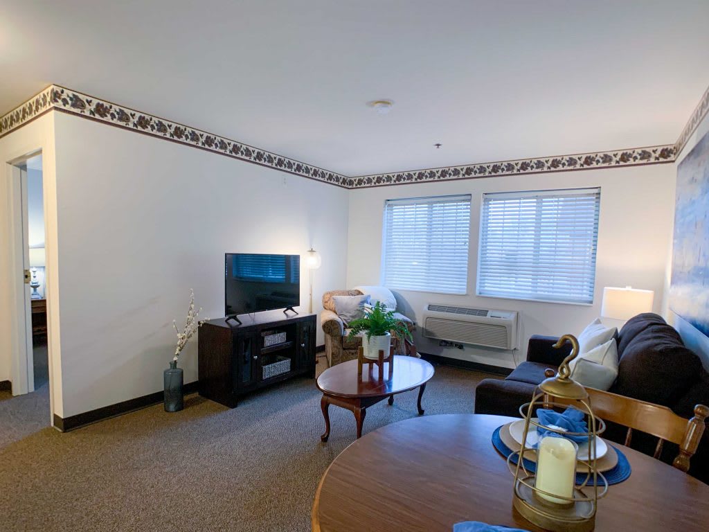 A cozy living room with a television, sofa, and coffee table near large windows.