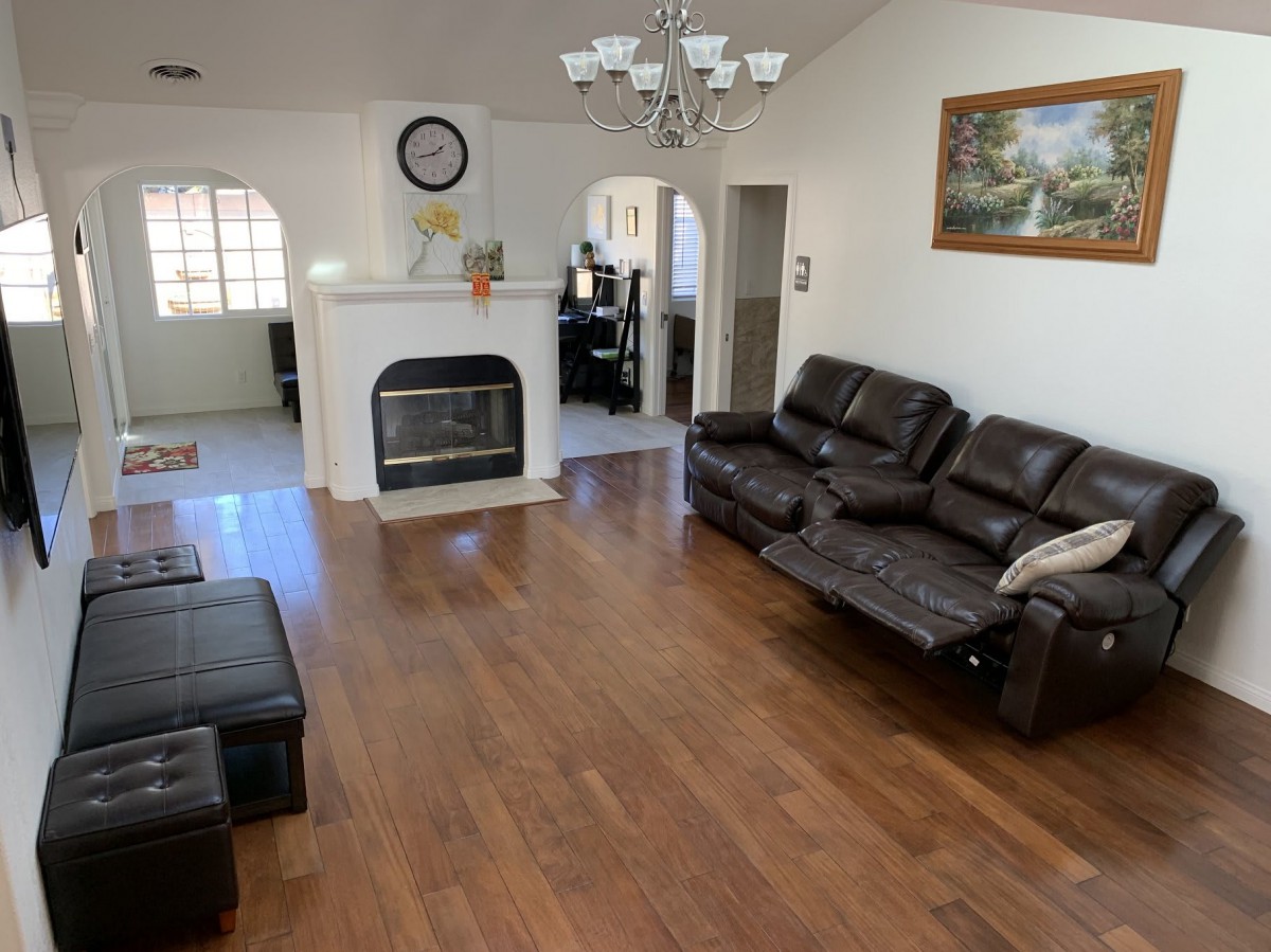 A spacious living room with hardwood floors, featuring a leather sofa, a fireplace, and a chandelier.
