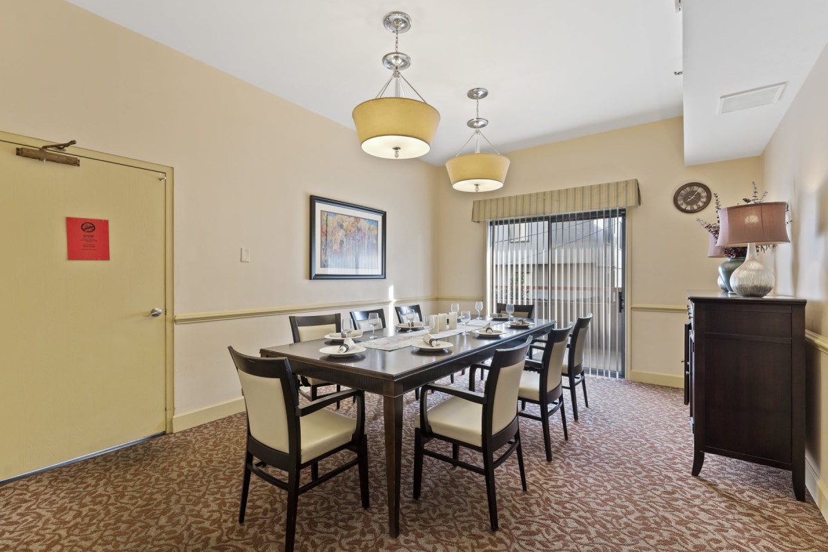 A well-set dining or conference room with a large table, surrounded by chairs, illuminated by two chandeliers.
