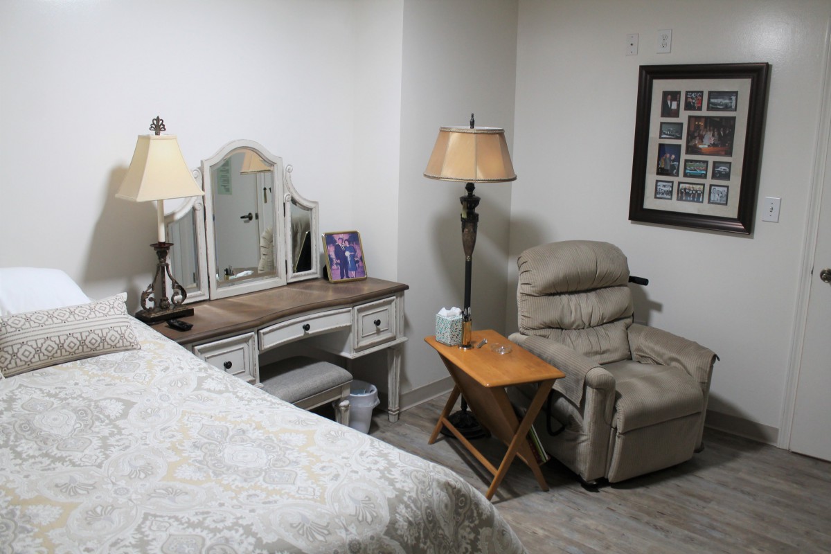 A cozy bedroom with a desk, armchair, and warm lighting.