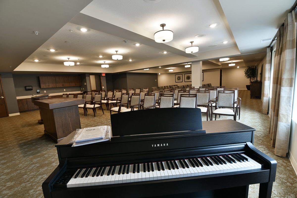 A spacious room featuring a piano and rows of chairs, illuminated by elegant ceiling lights.