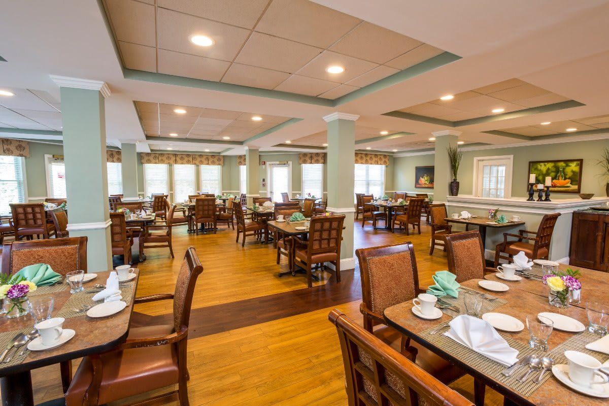 An elegant dining room with neatly arranged tables and chairs, featuring a warm wooden floor.