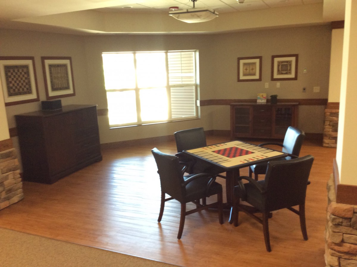 A cozy room with a wooden table and chairs, featuring large windows and decorative wall art.