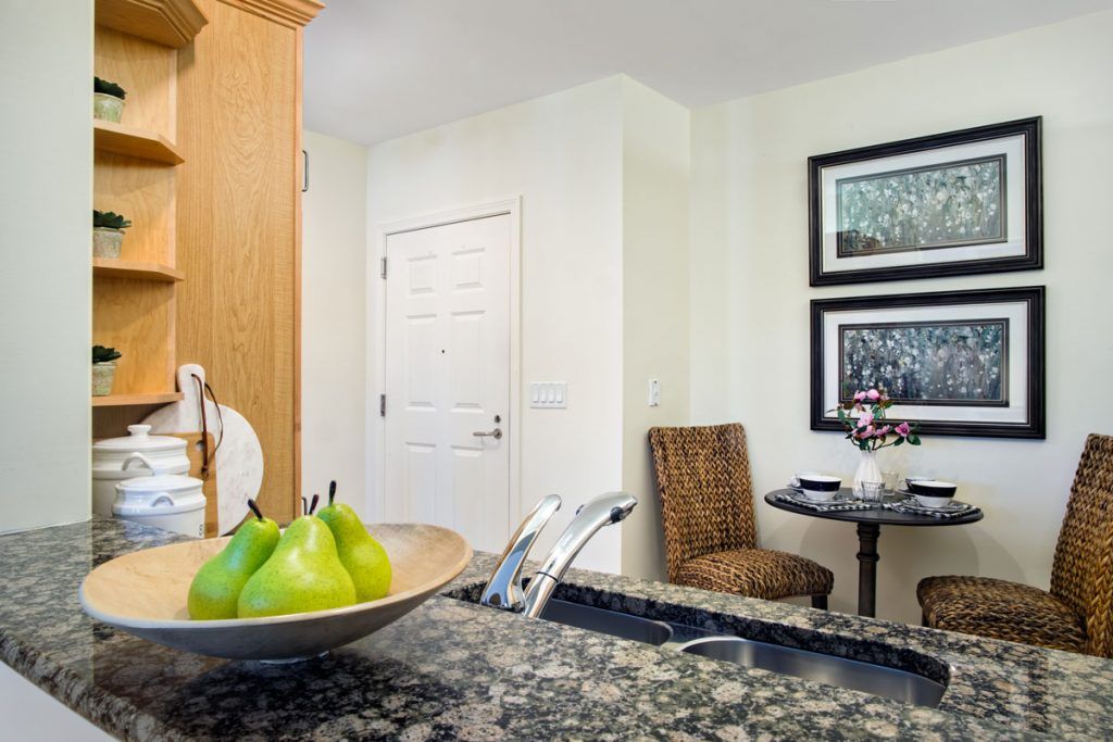 A cozy kitchen space with a bowl of pears on the counter and a small dining area with artwork on the wall.