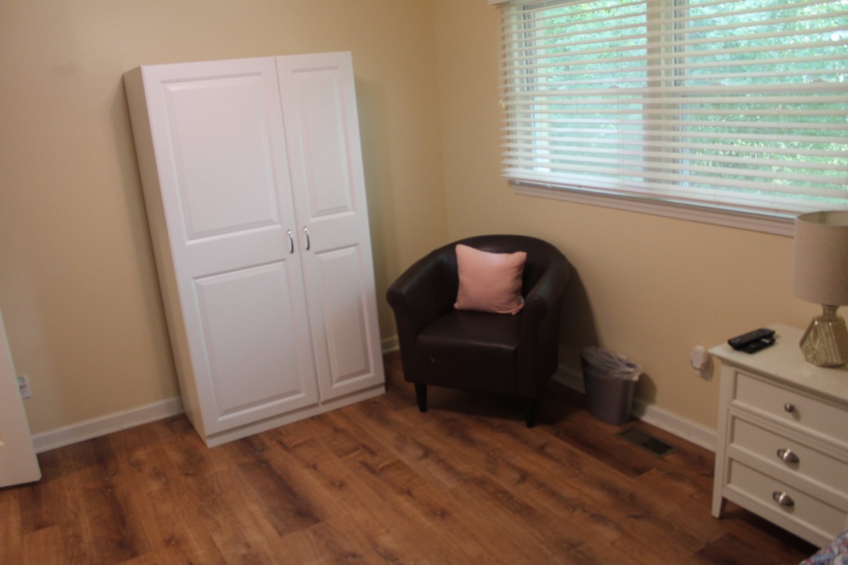 A cozy room featuring a white wardrobe, a black armchair with a pink pillow, and a wooden floor.