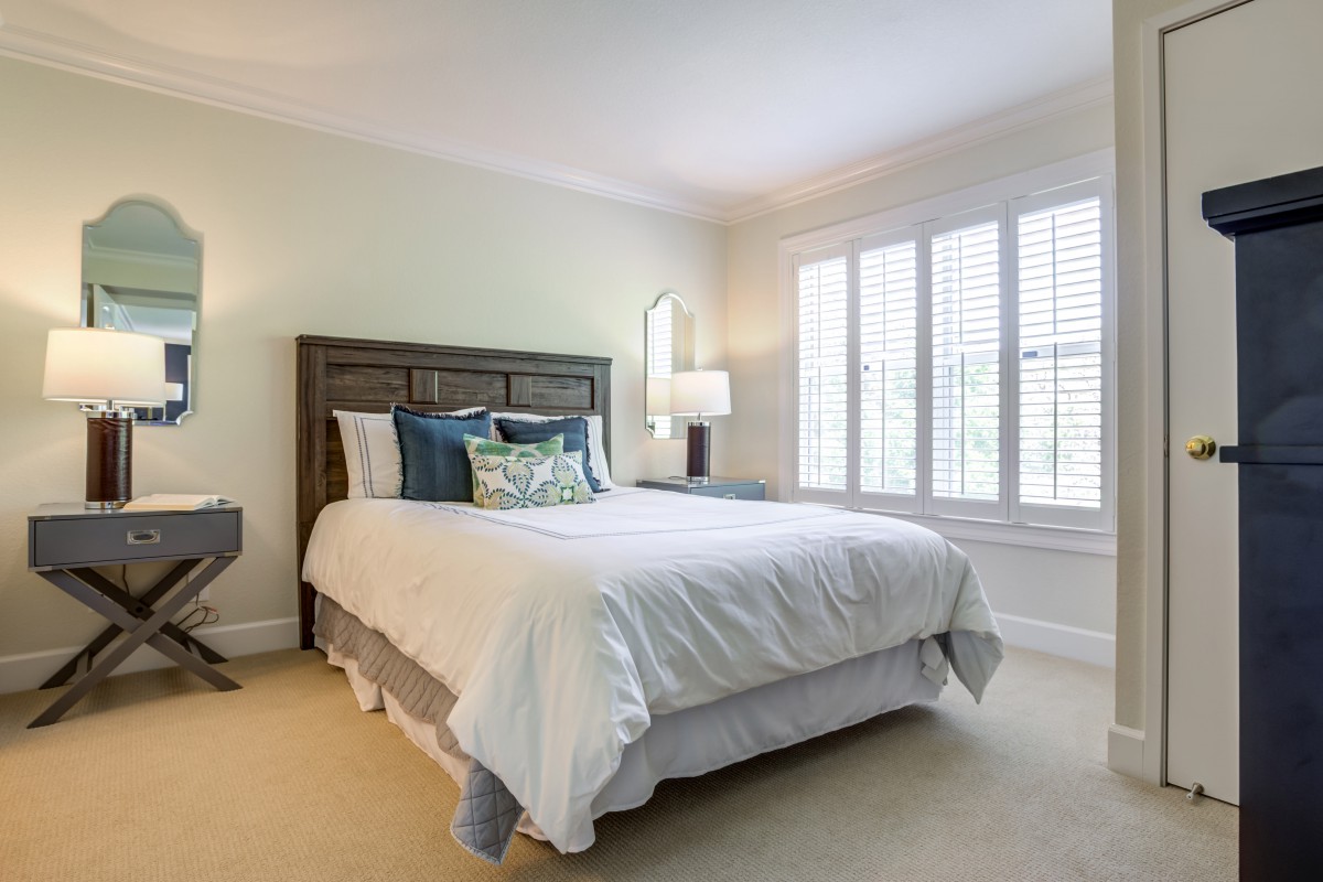 A cozy bedroom with a neatly made bed, soft lighting, and large windows.