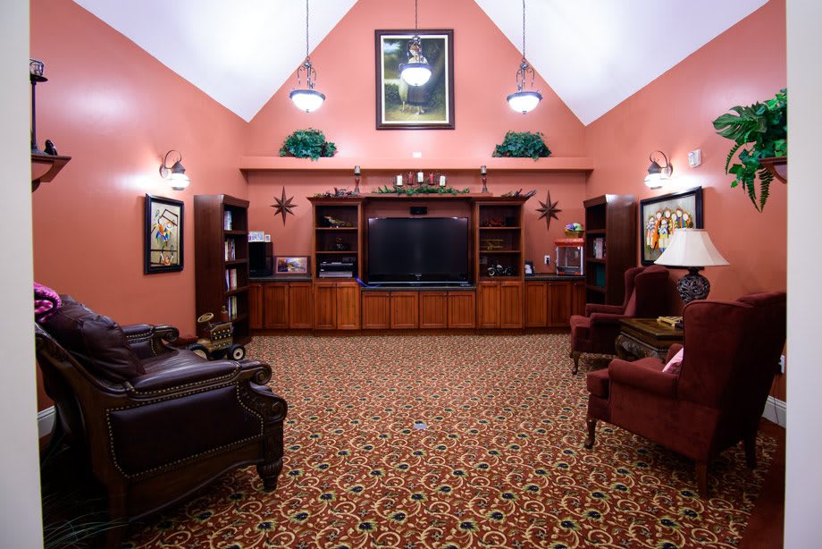 A traditional living room featuring a large entertainment center with surrounding bookshelves and comfortable armchairs on patterned carpet.