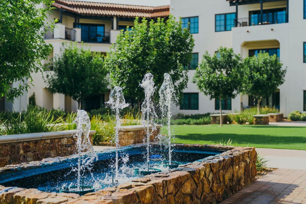 A serene courtyard featuring a bubbling fountain surrounded by lush greenery and residential buildings.