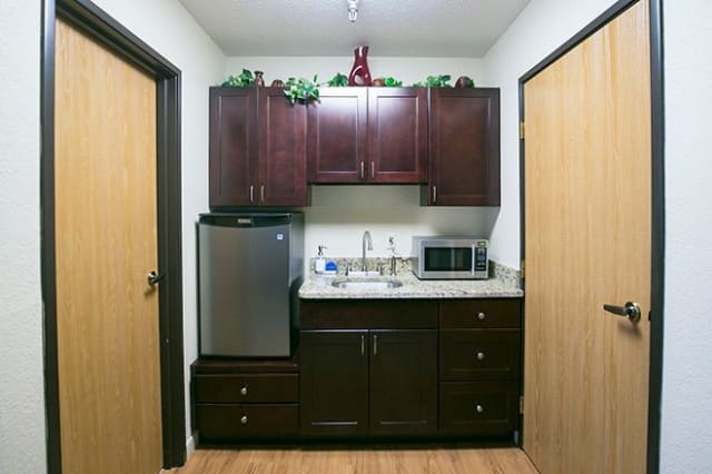 A compact kitchen setup with dark wood cabinets, a small refrigerator, a microwave, and a sink.