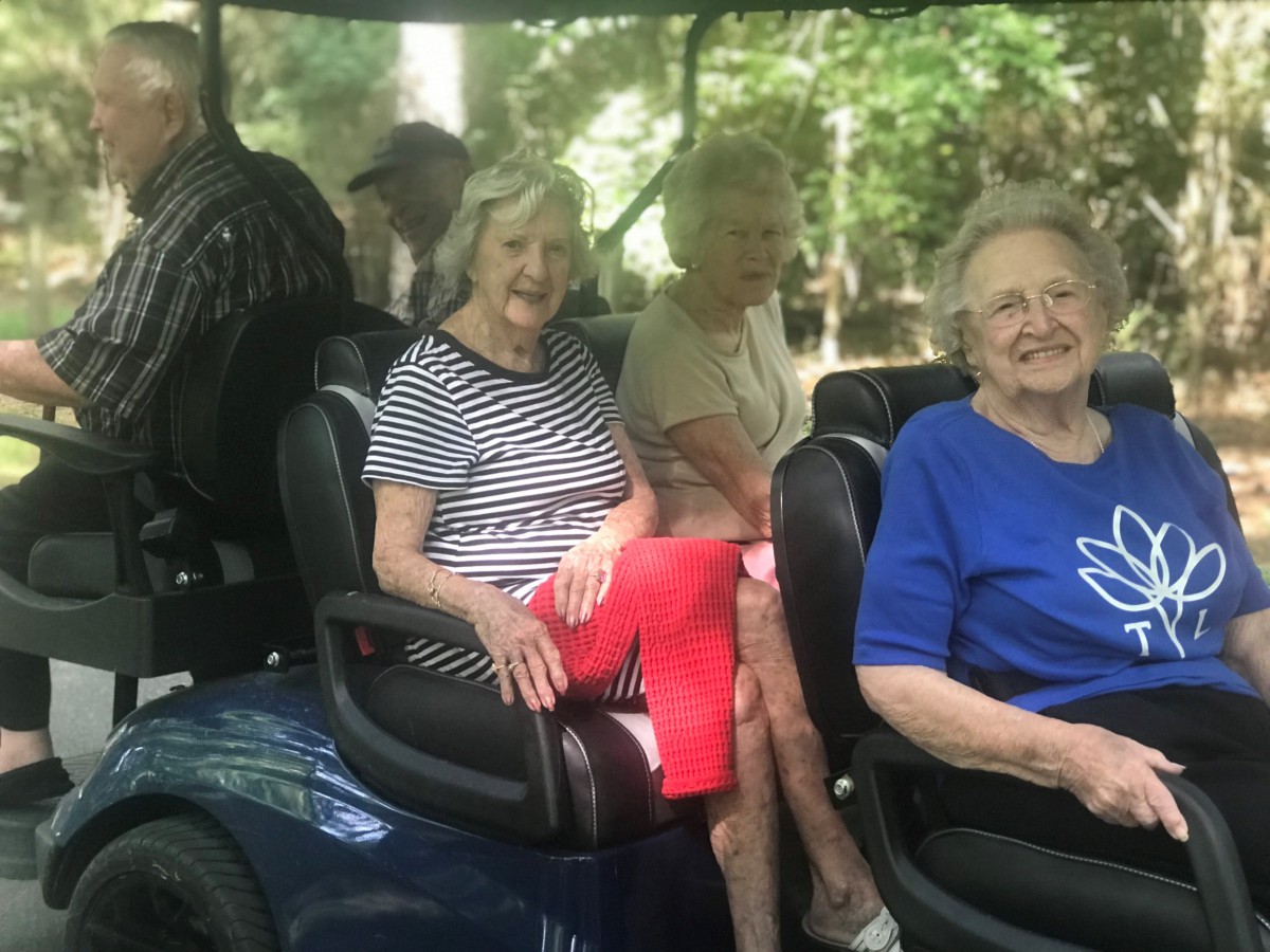 A group of seniors enjoying a leisurely ride on a golf cart in a wooded area.