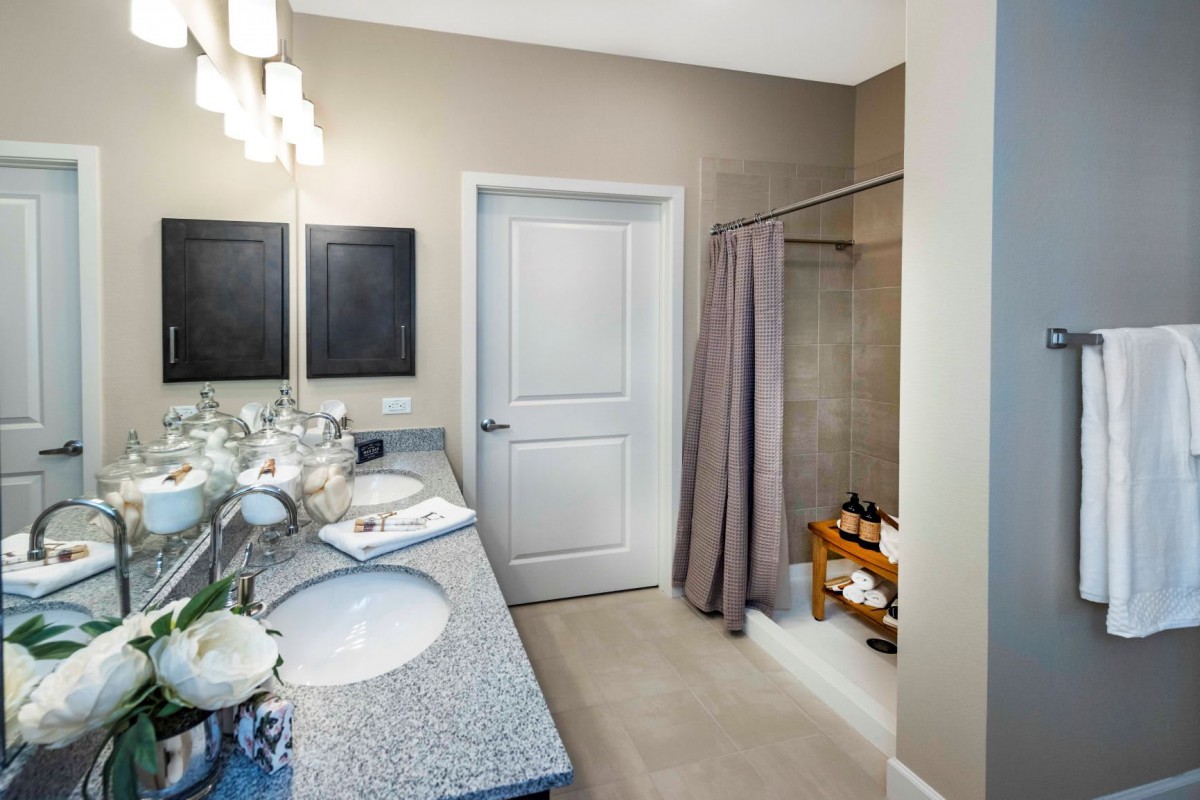 A modern bathroom featuring double sinks, a large mirror, and a shower with a curtain.