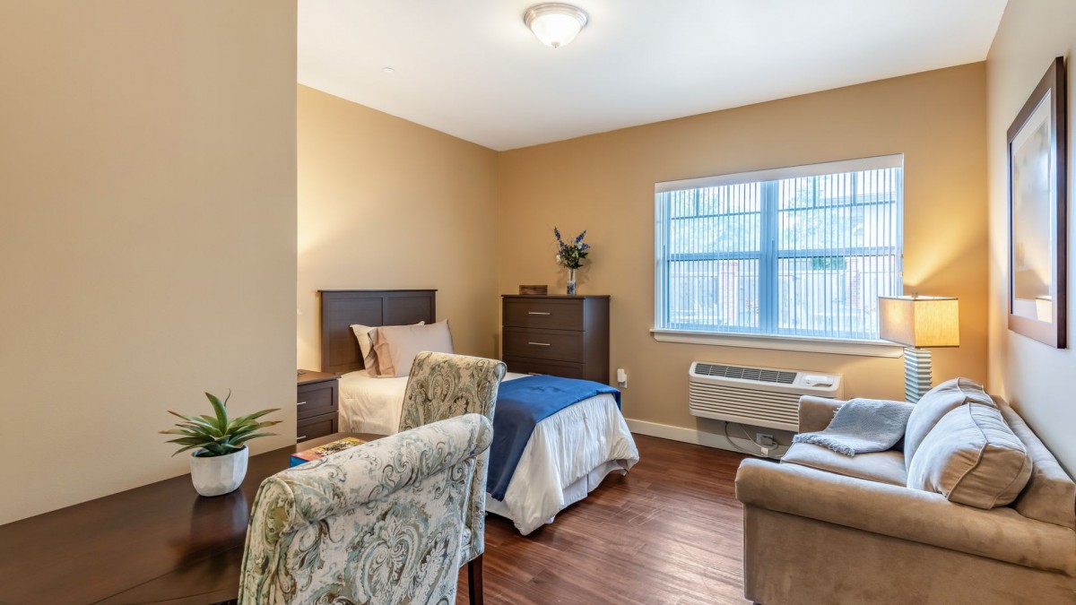 A cozy bedroom interior with a single bed, chair, dresser, and window.