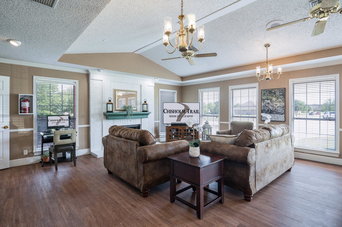 A spacious and elegantly designed living room featuring comfortable sofas, a chandelier, and large windows allowing natural light.