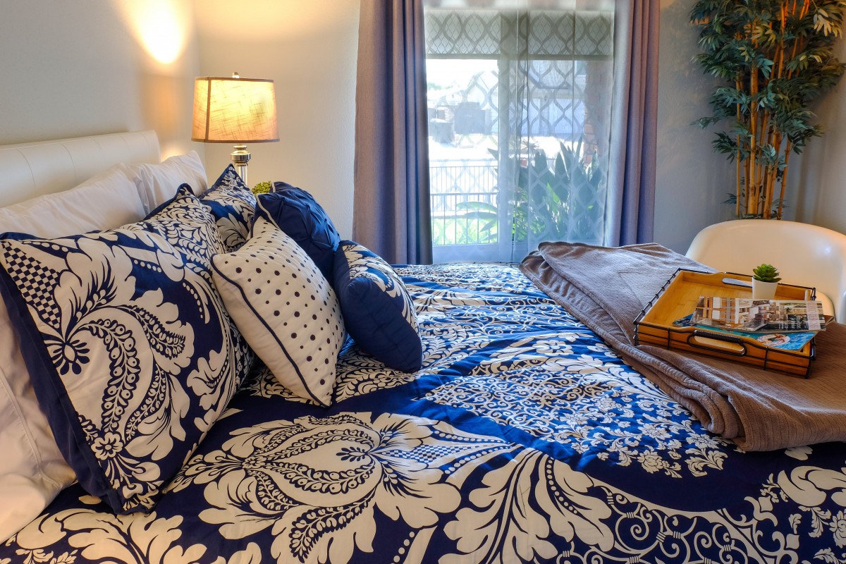 A beautifully decorated bedroom with patterned bedding and multiple pillows, softly lit by a bedside lamp.