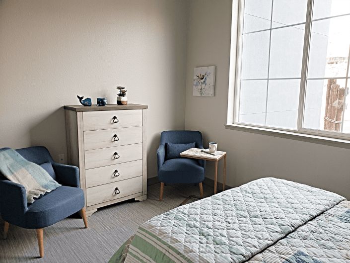 A cozy bedroom with a dresser, two armchairs, and a neatly made bed.