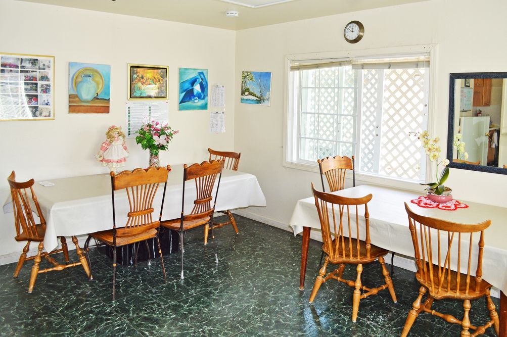 A cozy dining room with two tables, chairs, wall art, and a window letting in natural light.