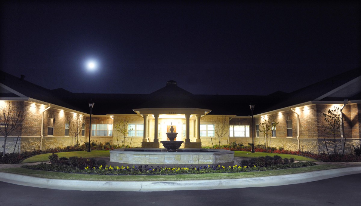 A well-lit building with a fountain in front, under a night sky with the moon visible.