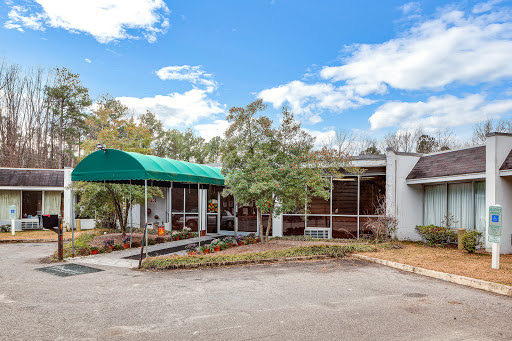 A view of a modern building with a green canopy, surrounded by trees under a bright blue sky.