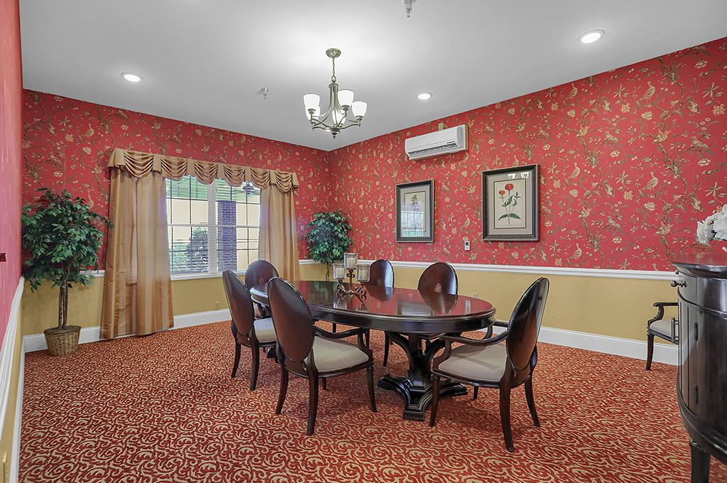 A cozy dining room with patterned wallpaper, featuring a round table and elegant chairs under a chandelier.