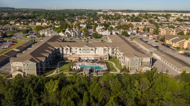 Aerial view of a residential apartment complex with a swimming pool, surrounded by greenery and suburban landscape.