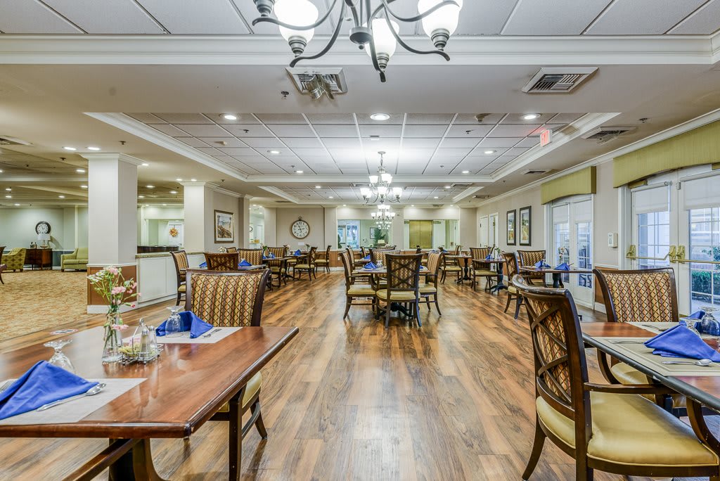 A spacious and elegantly designed dining area with wooden floors and chandeliers, featuring neatly arranged tables and chairs.