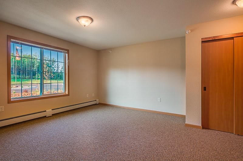 A vacant room with carpet flooring and a window letting in natural light.