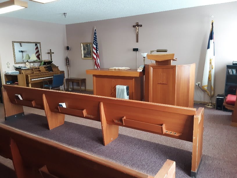 A small chapel with rows of wooden pews, a pulpit, and religious symbols.