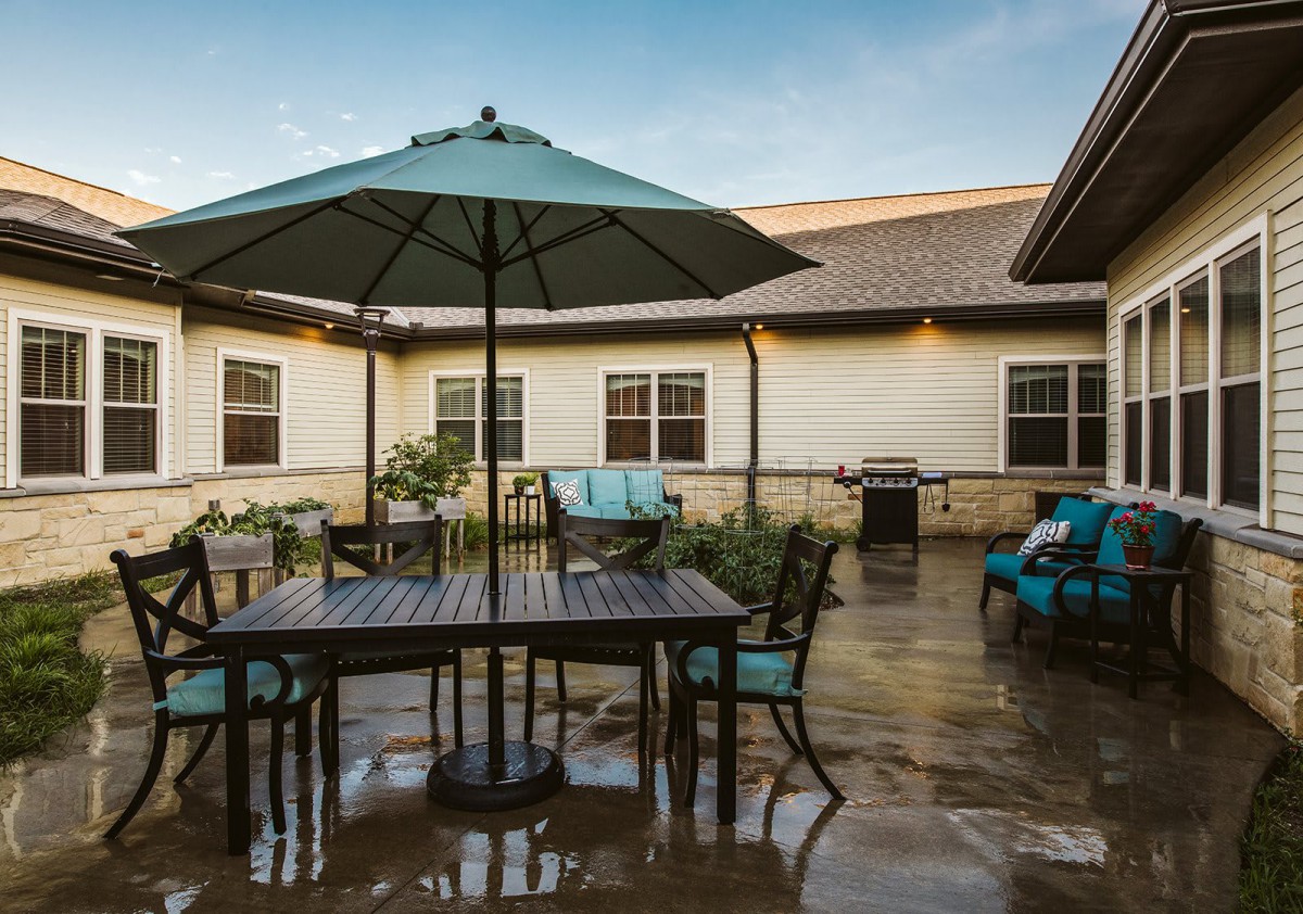 A tranquil patio area featuring outdoor furniture, including a table with an umbrella and chairs, set in a courtyard surrounded by a building exterior.