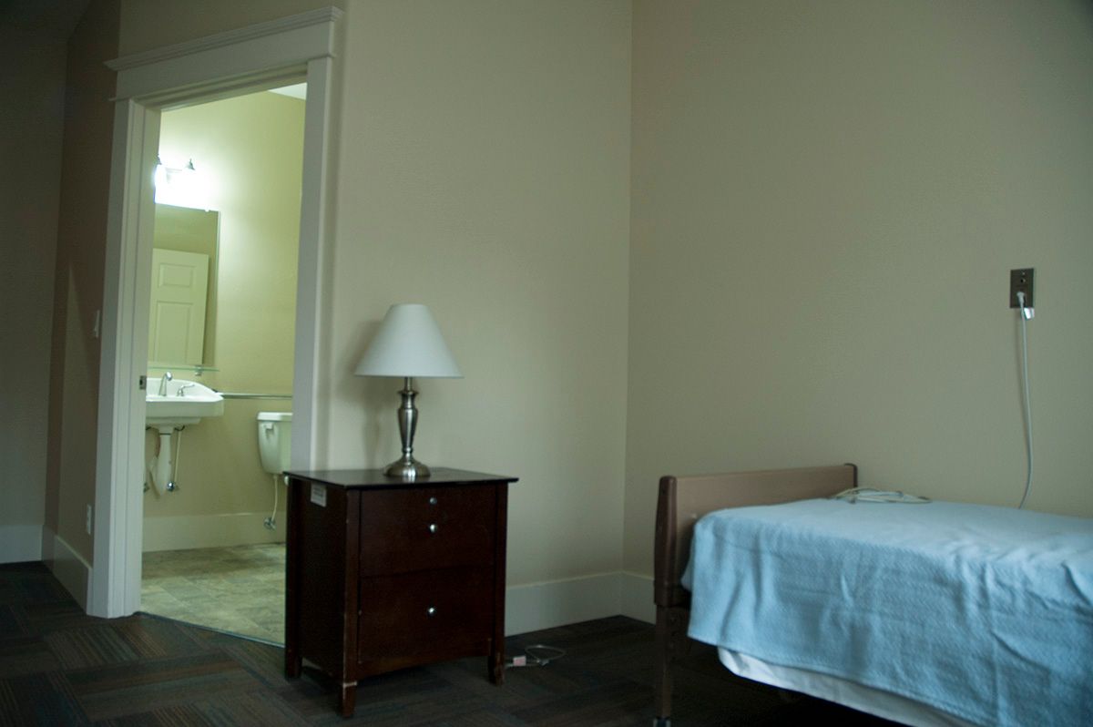 A simple bedroom with a bed, nightstand, and lamp, leading to an adjoining bathroom.