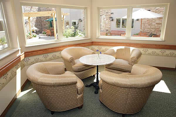 A cozy seating area with four upholstered chairs around a round table, surrounded by windows.
