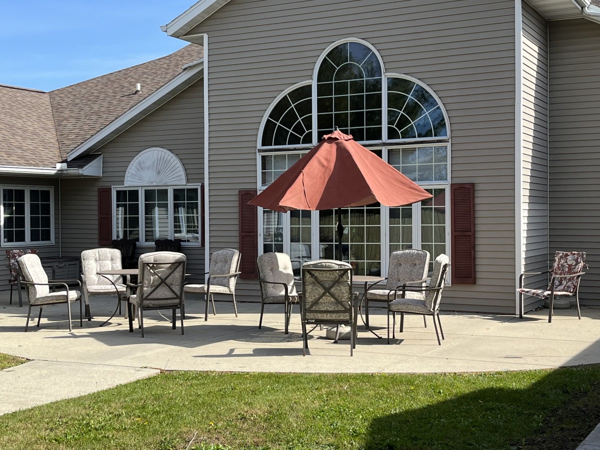 A sunny patio with outdoor furniture and a red umbrella in front of a house.