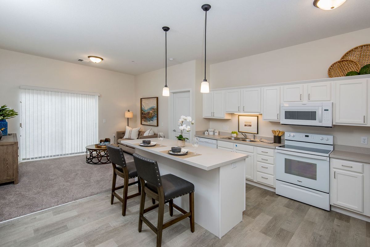 A modern kitchen with white cabinets, featuring an island with bar stools and pendant lighting.