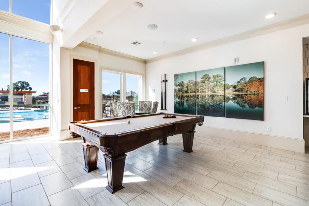 A bright game room featuring a pool table, large windows, and wall art.