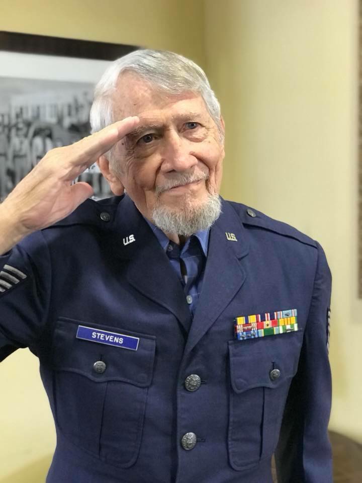 An elderly man in a military uniform giving a salute.
