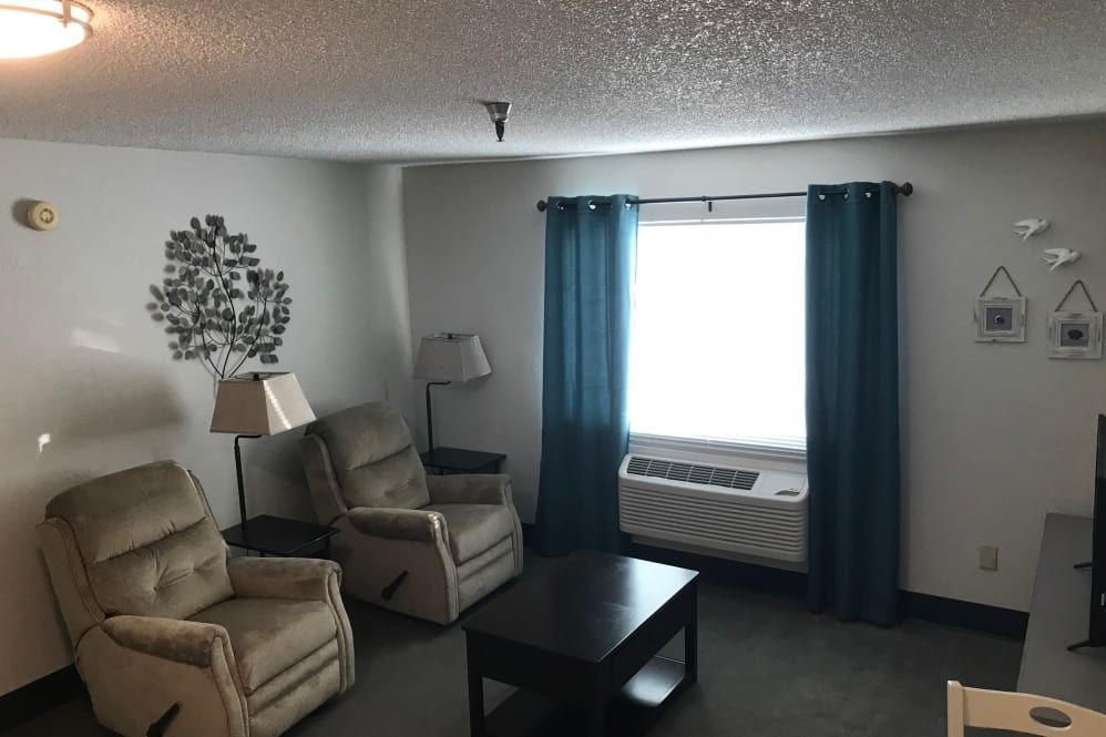 A cozy living room with two armchairs, a small coffee table, floor lamps, and a window with blue curtains.