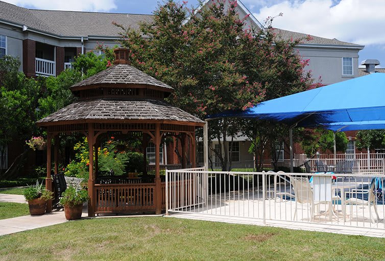 A scenic outdoor area with a wooden gazebo and a shaded pool surrounded by trees.