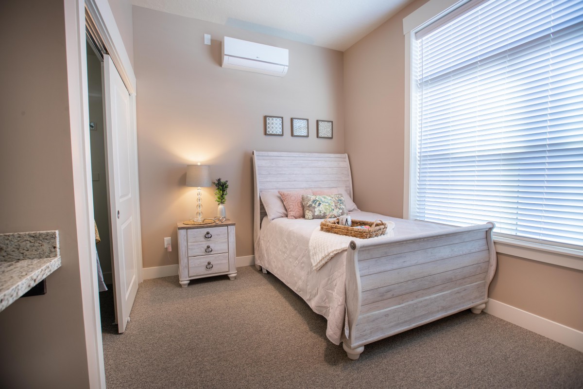 A cozy and minimalist bedroom with a neatly made bed, nightstand, lamp, and window blinds.
