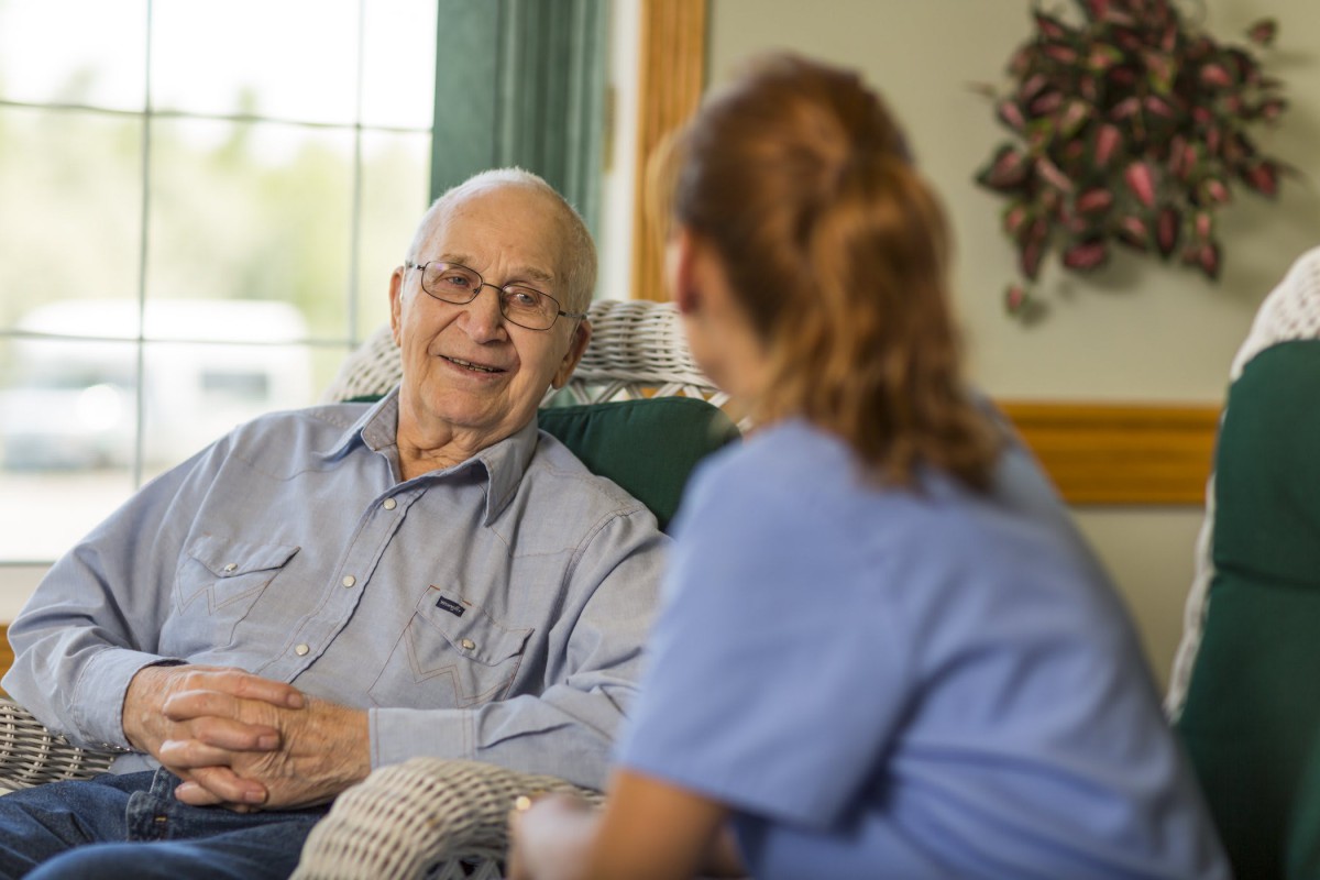 An elderly man having a conversation with a caregiver in a home setting.