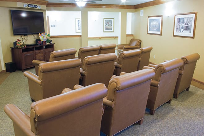 A cozy theater room with rows of comfortable leather chairs facing a large screen.