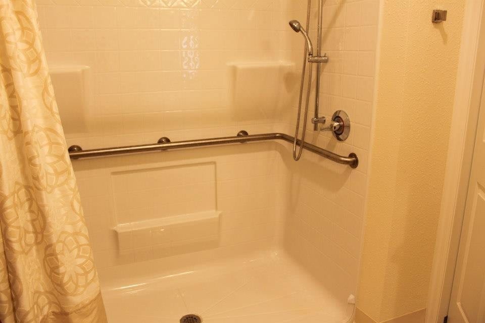 A bathroom shower with accessibility grab bars and a handheld showerhead.