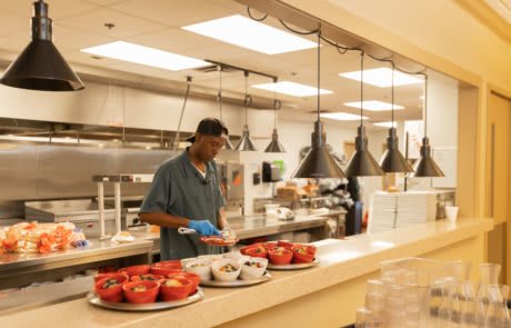 A man serving food in a cafeteria kitchen.