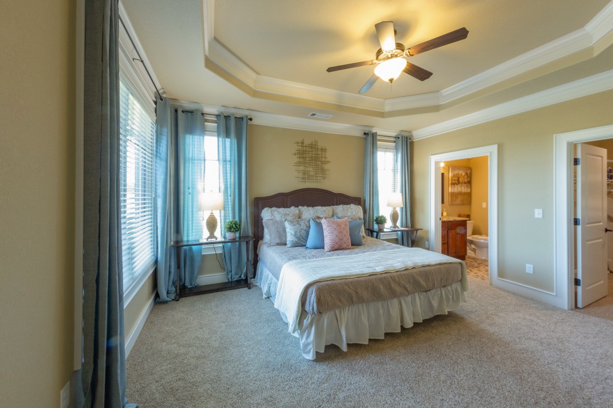 A spacious and well-decorated bedroom with a large bed, ceiling fan, and ample natural light.