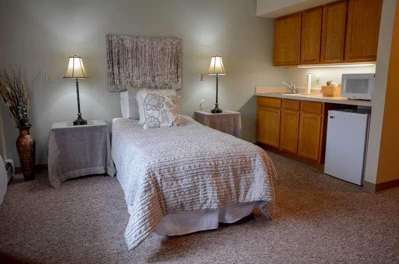 A cozy bedroom featuring a single bed with a neutral color scheme, two lamps on bedside tables, and built-in cabinets.