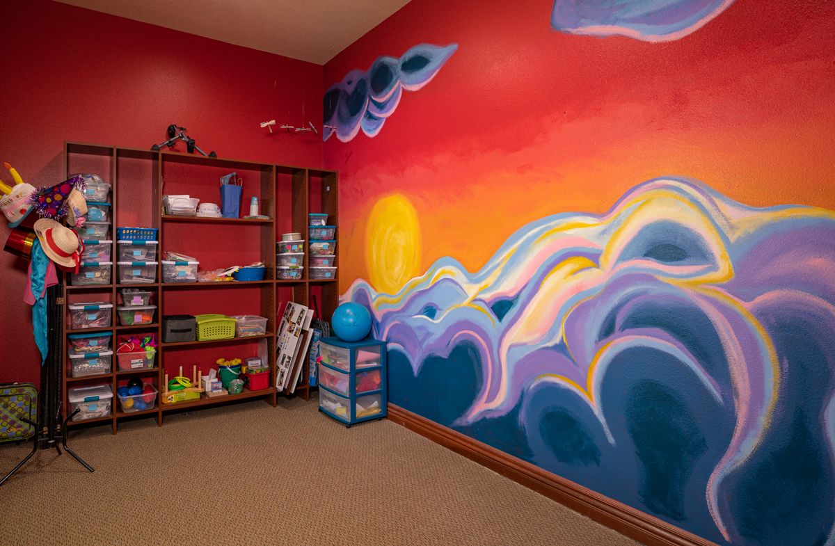 A vibrant room featuring a colorful mural of a sunset with clouds, accompanied by organized shelving.