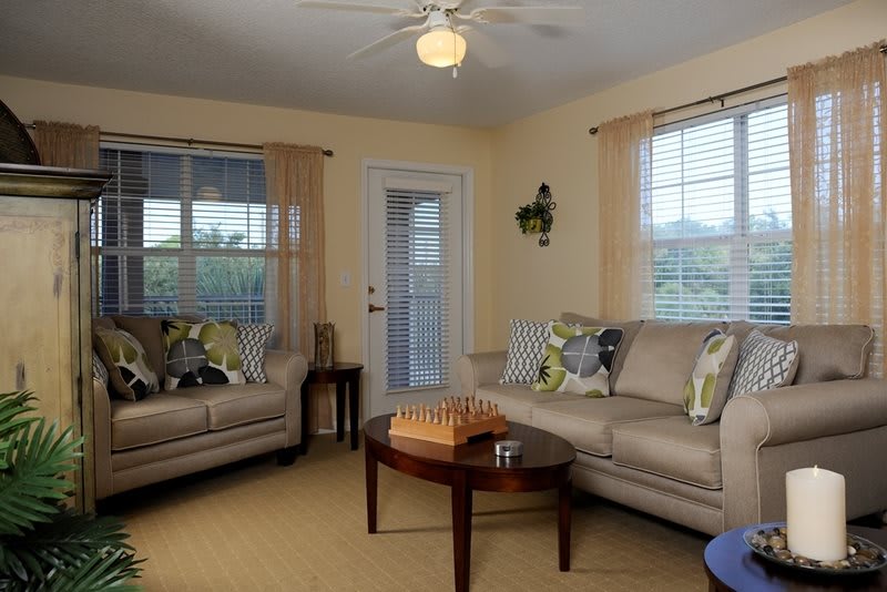 A cozy living room featuring beige sofas, a wooden coffee table, and windows with curtains.
