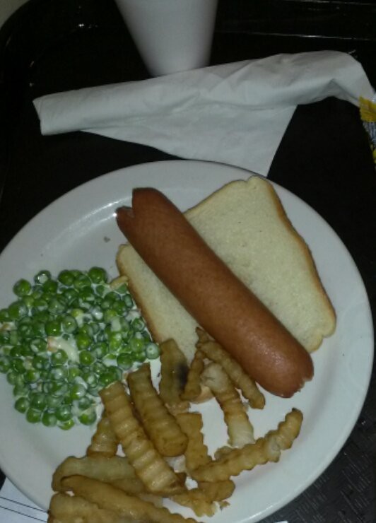 A meal consisting of a hot dog on bread, crinkle-cut fries, and peas on a plate.