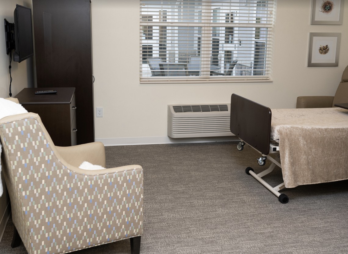 A clean and well-organized hospital room with a bed and a comfortable chair near a window.